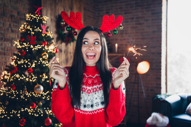照片中的女孩穿着红色印花套头衫，手拿孟加拉灯棒，在室内庆祝新年，欢呼雀跃图片下载