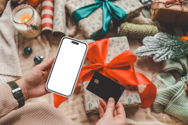年轻女子手持信用卡和礼品盒，背景是圣诞装饰和礼物，特写。圣诞节和新年在网上购物，用信用卡付款图片下载