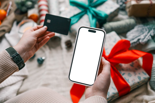 年轻女子手持信用卡和礼品盒，背景是圣诞装饰和礼物，特写。圣诞节和新年在网上购物，用信用卡付款图片下载