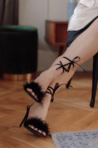 剪短的照片，一个女人坐在椅子上，穿着黑色的高跟鞋，凉鞋上装饰着蓬松的羽毛和鞋带。图片下载