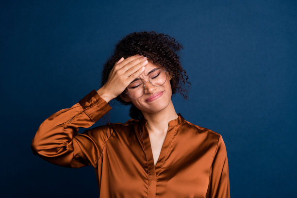 照片上疲惫不堪的女人穿着棕色丝绸衬衫，戴着眼镜，手前额高温孤立的蓝色背景图片下载