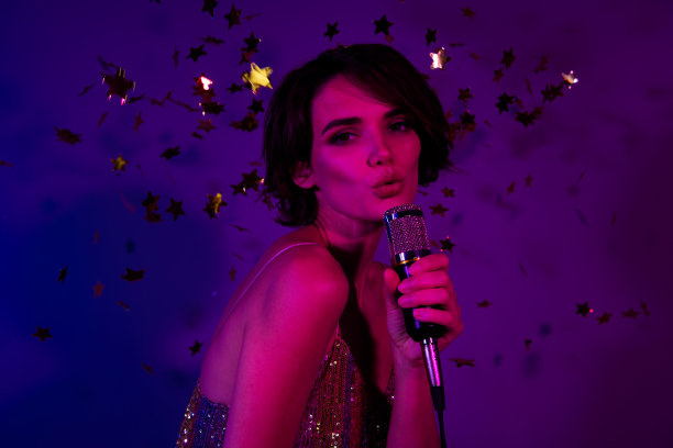照片中，惊艳的流行女歌星在夜总会舞台活动场合演唱，背景是明亮的霓虹灯色图片下载