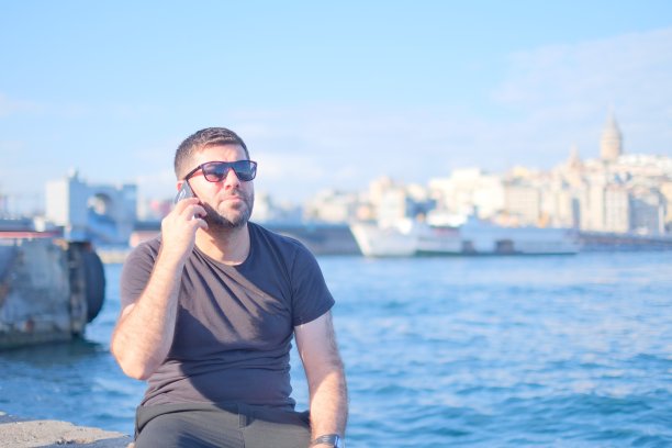 一个男人在打电话时笑的照片，背景是大海。图片下载