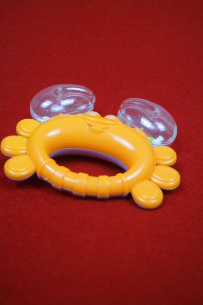 黄色螃蟹形状的儿童玩具，里面有小球，发出很大的声音。红色背景图片下载