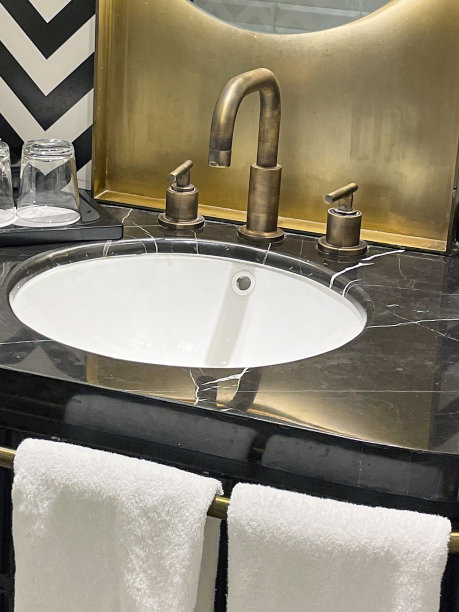 特写照片:折叠的白色毛巾挂在盥洗台的毛巾架上，大理石托盘上有倒扣的水杯，大理石浴室柜台上有单色之字形图案的墙砖，墙上装着镜子图片下载