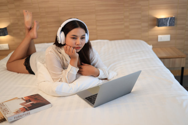 快乐的美女在家里的床上听音乐和通过笔记本电脑在线工作图片下载