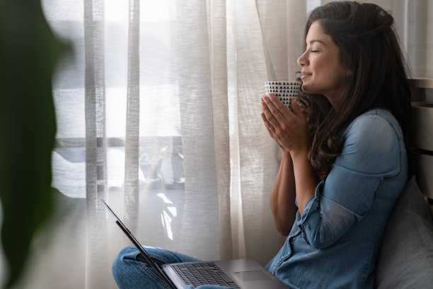 美丽的微笑的年轻女子坐在家里舒适的窗角，喝着咖啡，放松图片下载