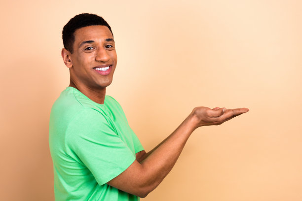 照片中，迷人的年轻男子双手捧空，穿着时髦的绿色衣服，孤立在米色背景上图片下载