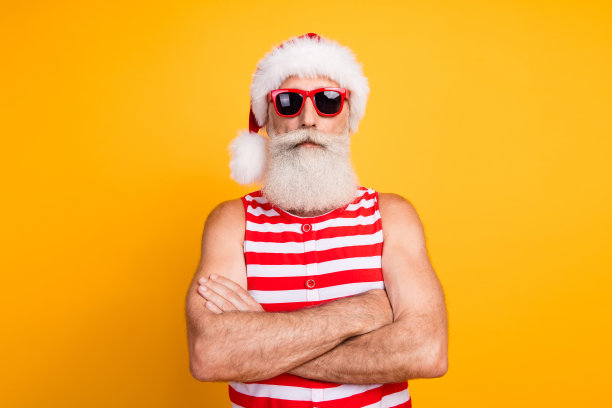 照片中酷酷严肃的老人戴着新年泳装，帽子，太阳镜双臂折叠，旅行孤立的黄色背景图片下载