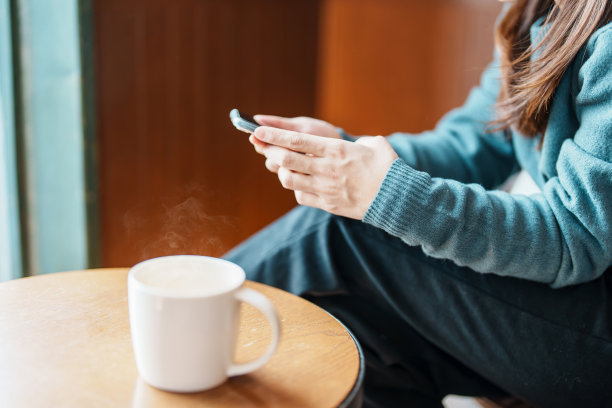 女性在早上喝热咖啡或热茶时使用智能手机。商务、网上购物、网上银行和转账的概念图片下载