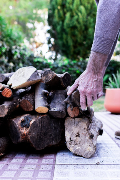 一个老人的手在家里堆柴火的特写照片。图片下载