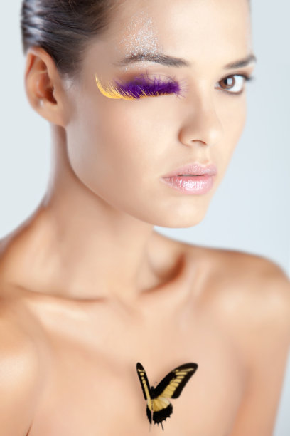 模特用紫色羽毛制成的假睫毛，闪亮的嘴唇上有蝴蝶的创意妆容图片下载