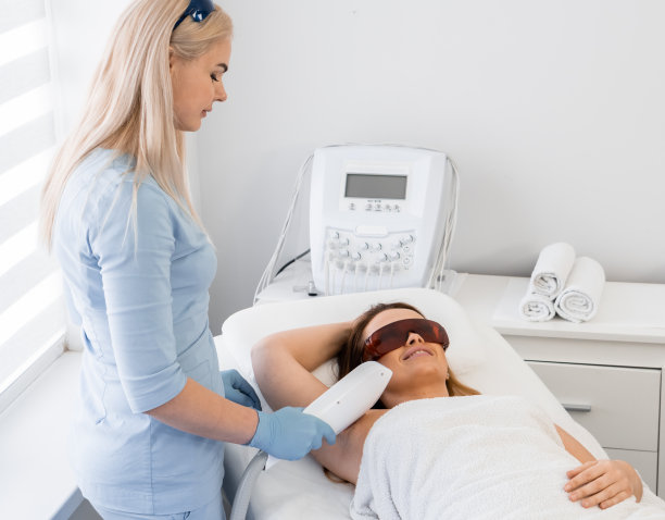 经验丰富的美容师和光脱毛程序，以光滑的皮肤和深度舒适的美容院。妇女在手术过程中休息和放松。病人躺下微笑图片下载