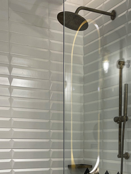 特写照片:折叠的白色毛巾挂在玻璃淋浴间门上的毛巾架上，大黄铜淋浴头，大理石浴室柜台，单色之字形墙砖图片下载