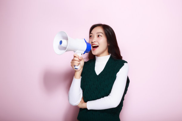 一名亚洲女子站在浅粉色背景前，拿着扩音器摆姿势。图片下载