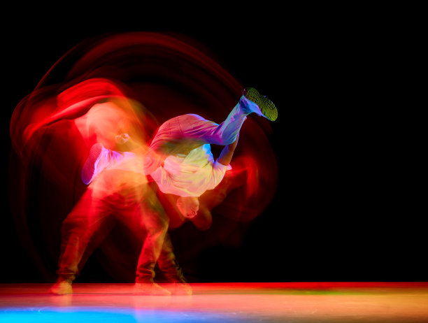 年轻的运动员，跳街舞的b-boy，一只手跳霹雳舞，在霓虹灯的黑色背景下抬起腿图片下载