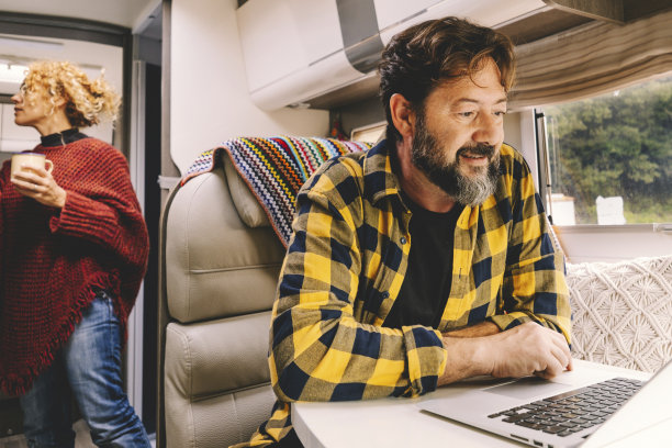 成年夫妇旅行，享受假日假期或vanlife的生活方式——快乐的男人在桌子上的笔记本电脑上工作，女人在车里寻找东西——户外自然图片下载