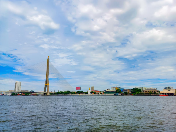 这张照片上，一座吊桥优雅地横跨在宁静的河流上，在广阔的蓝天下，引发了一种令人惊叹的威严感，工程奇迹与自然的宁静融为一体。图片下载