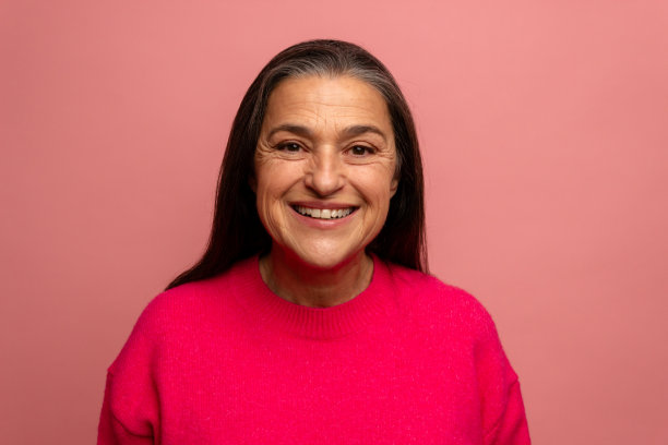 在粉红色的背景下，一个快乐的老年妇女对着相机微笑的肖像图片下载