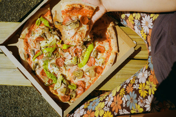 正上方的照片是夏日里坐在长凳上的女人从外卖盒里拿着一片披萨图片下载