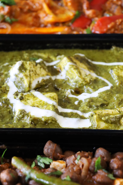 全画幅图片精选印度外卖菜黑色塑料，一次性食品容器，食谱包括，卡代鸡，Palak奶酪(白干酪和菠菜泥)，Pindi辣椒酱(鹰嘴豆咖喱)，高架视图图片下载