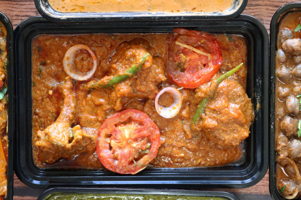 精选的印度外卖食品图片，装在黑色塑料的一次性食品容器里，食谱包括:Chicken Bhuna, Palak paneer(白干酪和菠菜泥)，Pindi chole(鹰嘴豆咖喱)，Kadai Chicken和Dal makhani(黑扁豆咖喱)。图片下载