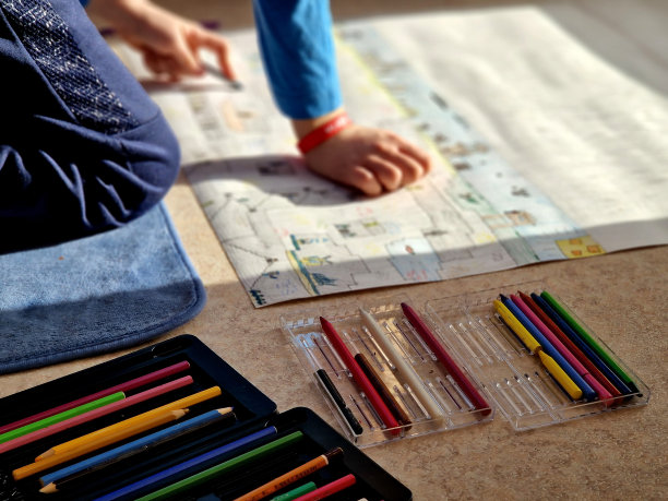 一个男孩坐在公寓的地板上，在一张大纸上用立方体画出他的幻想世界。矿山和崩落在2d。墨盒里有很多蜡笔就在手边。图片下载