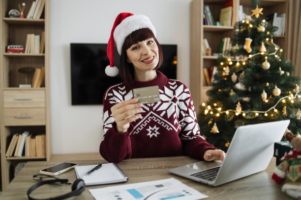 戴圣诞帽的白人女性坐在办公桌前，背景是圣诞树图片下载