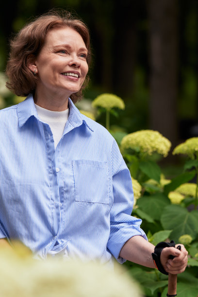 有魅力的成熟女人在公园里拄着北欧步行杆。一位老妇人走在公园的小巷里。穿蓝衬衫的黑发中年女性，笑得很开心。老年人积极的生活方式。图片下载