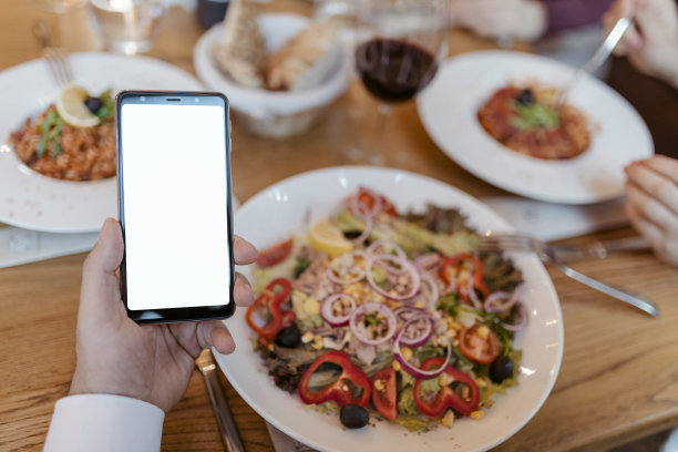 一名女子在餐厅拿着智能手机对着食物的裁剪照片图片下载