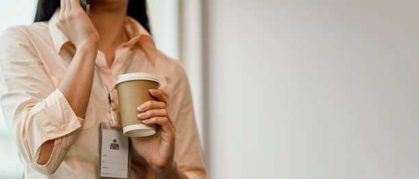 年轻女职员拿着一杯热咖啡，边走边打电话图片下载