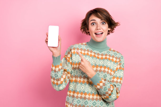 照片震惊年轻女孩棕色鲍勃头发穿高领冬装点手指数码屏幕存储孤立的粉红色背景图片下载