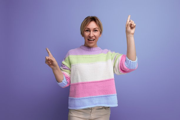 迷人的金发年轻女子指着墙上的紫色背景与复制空间图片下载