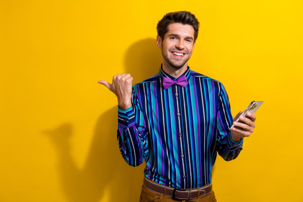 带着领结、笑容满面的家伙的肖像，手持智能手机，在充满活力的黄色背景下，对着商店的空旷空间图片下载