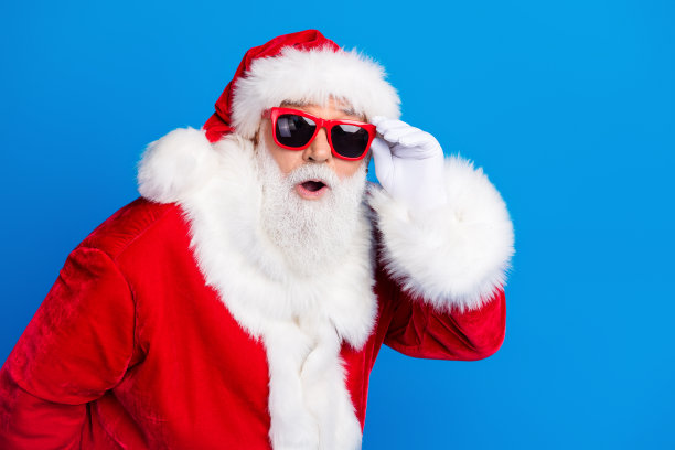 老人的照片肖像触摸眼镜惊讶地穿着时尚的圣诞老人服装外套孤立的蓝色背景图片下载