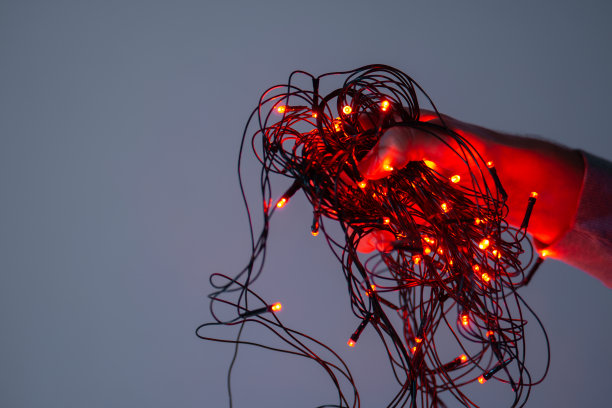 男性手握纠结的红色圣诞彩灯的特写图片下载