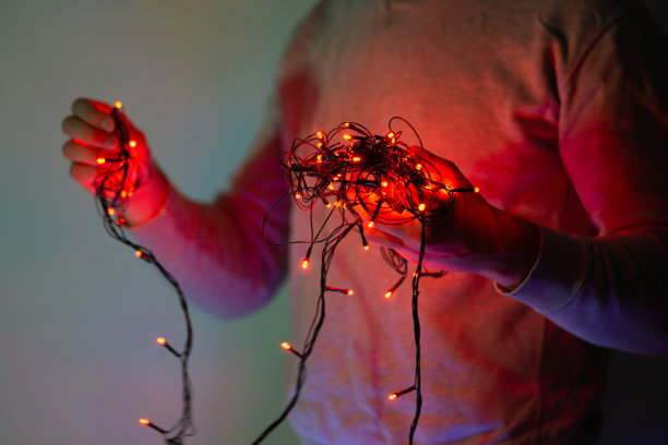 男手拿着纠结的圣诞彩灯串，男手解开五颜六色的圣诞彩灯串图片下载