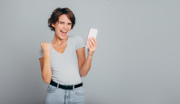 近距离照片尖叫的好消息女孩与漂亮的短发和完美的皮肤前灰色的颜色拿着她的手机，兴奋地微笑真诚。赢，赌，乐透，好消息图片下载