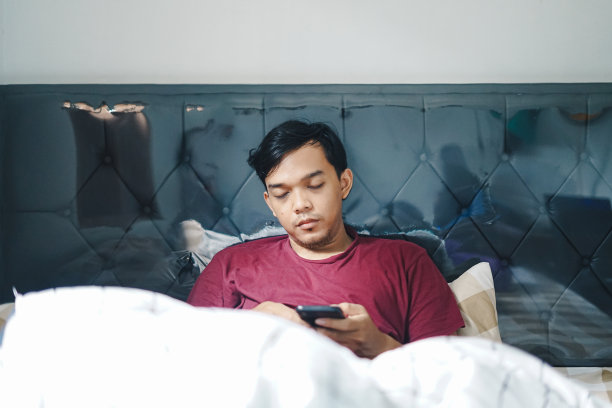 亚洲男子躺在床上拿着智能手机睡着的照片图片下载