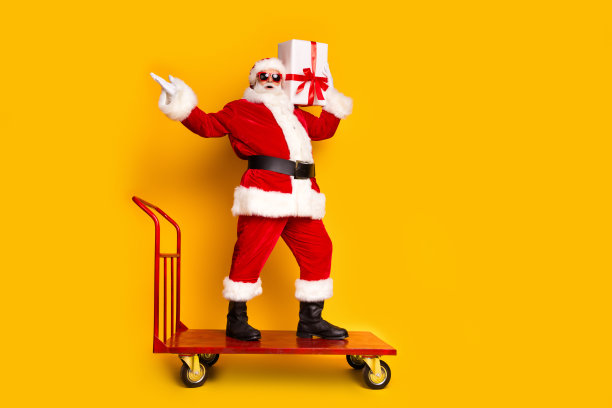 疯狂圣诞老人的全身照片站市场手推车持有圣诞前夕礼盒空空间孤立的黄色背景图片下载