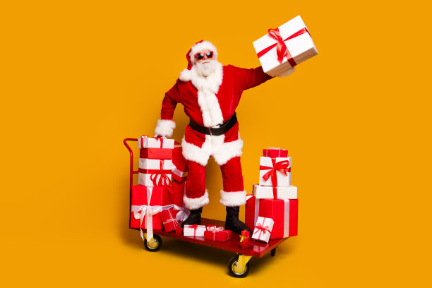 古怪的圣诞老人站在手推车hold新年礼盒孤立黄色背景的全长照片图片下载