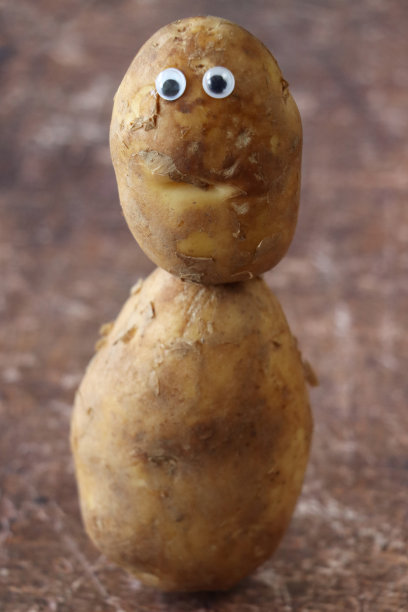 有趣的特写形象，由小土豆头和大土豆身体上平衡的大眼睛组成的卡通人物，棕色的背景，儿童健康饮食，幽默的概念，重点放在前景上图片下载