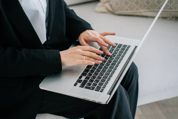 剪短的照片里，一个女人在家里用笔记本电脑打字，穿着黑色西装坐在沙发上。女商人用手提电脑给合伙人写信。财务人员，在家办公。图片下载