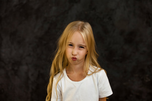 肖像的皱眉封面女孩儿童模特在白色t恤表达情绪，皱着眉头看着相机。愤怒的6岁孩子在摄影棚拍摄的黑色照片前摆姿势。孩子的情感概念。复制广告文本空间图片下载
