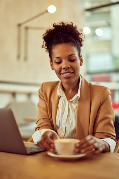 一个美丽的非洲女人的照片，在咖啡店工作，喝着卡布奇诺。图片下载