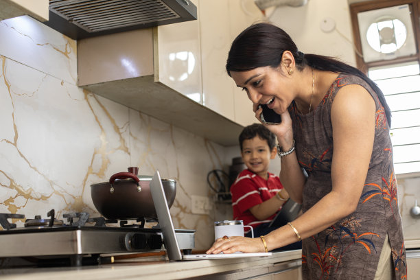 母亲在厨房工作，儿子坐在操作台上图片下载
