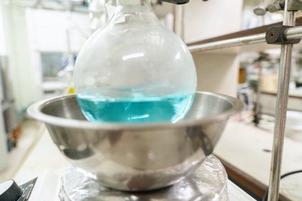 圆形的烧瓶中装满蓝色的溶液，准备加热，在现代实验室的油浴中进行化学反应。实验室和研发。加热浴中的化学合成过程。医学综合。图片下载