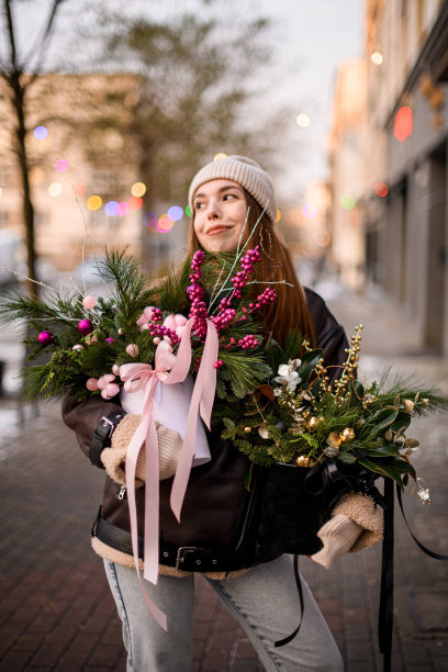 微笑的直发女孩，穿着夹克，戴着帽子，手里拿着装饰好的冷杉枝花束图片下载