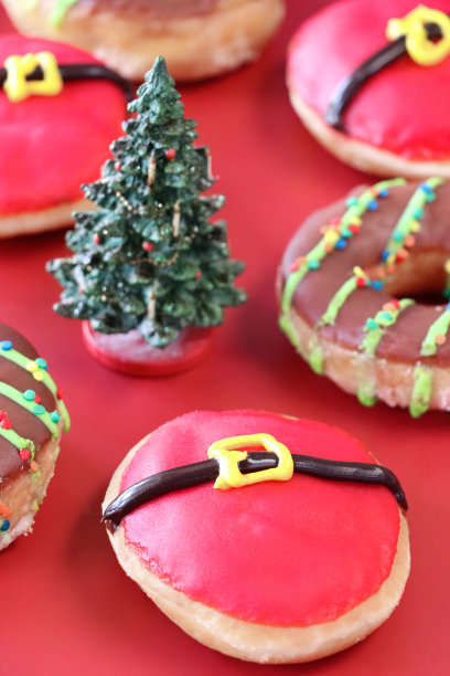 模型圣诞树特写图片，有一批圣诞老人肚皮糖冰甜甜圈和巧克力釉面环甜甜圈，油炸面团甜点装饰有红色糖霜和扣带细节，红色背景，前景提升焦点图片下载