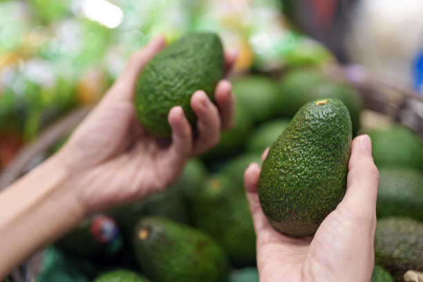 在一张特写照片中，一位顾客正在杂货店挑选牛油果。图片下载
